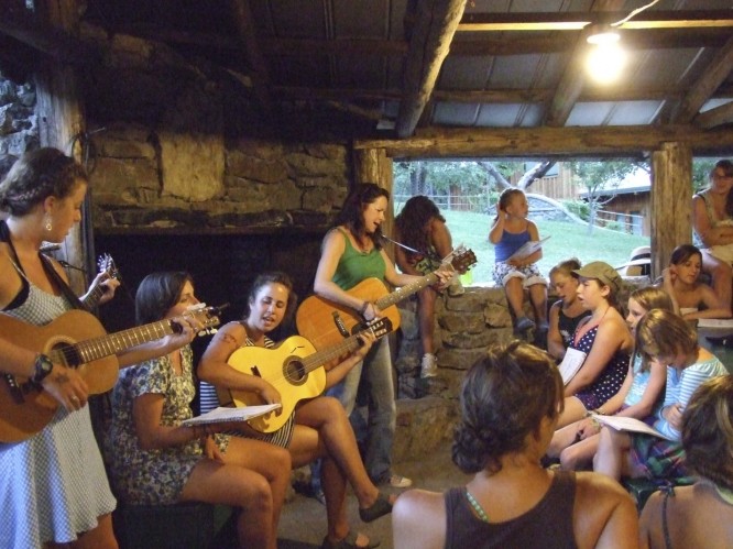 counselors and campers play guitar and sing in front of a large fireplace