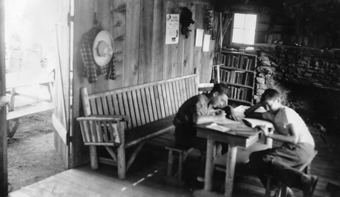 Two young people read at a table inside Leedy Lodge, 1930s