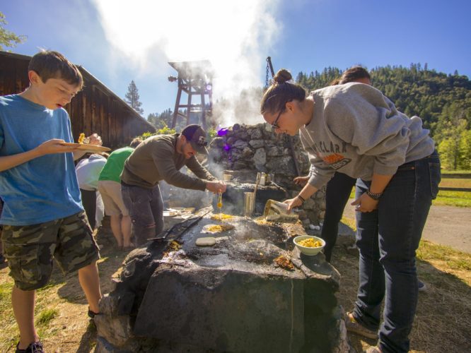 Campers and staff cook eggs and pancakes on a wood fired griddle