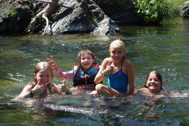 Four smiling girls give thumbs up from the middle of the river