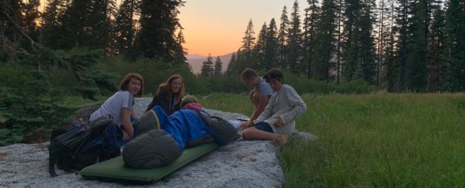 Campers relaxing in sleeping bags at dusk in the Trinity Alps
