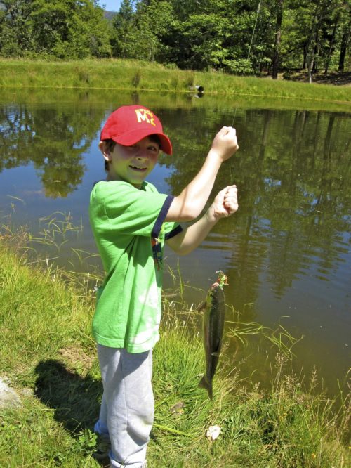 Camper holds up fish on fishing line, next to a pond