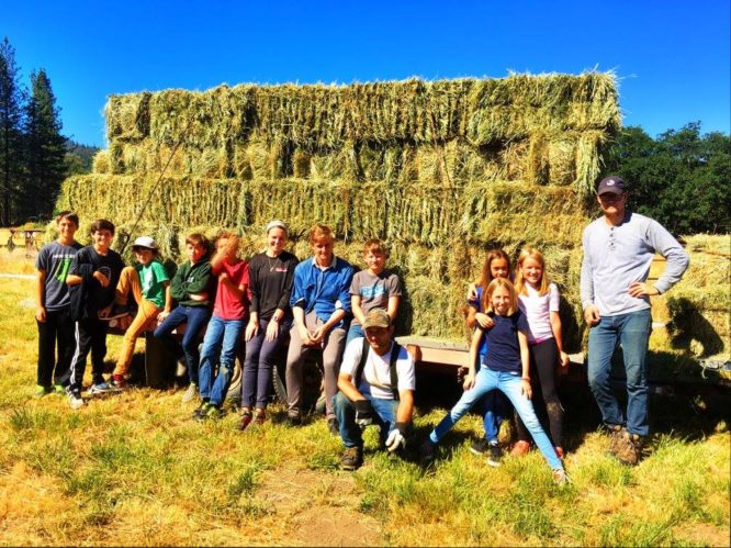 Campers and counselors pose in front of a full hay truck