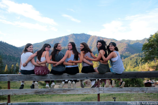 Seven girls sit smiling on a fence